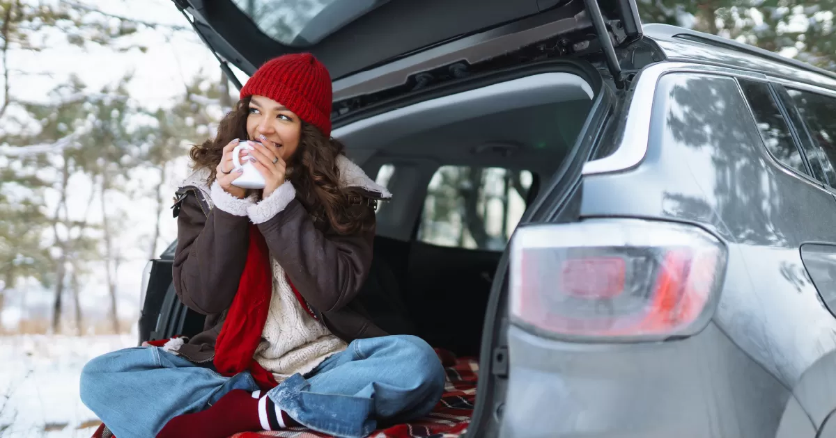 Woman sitting in the back of her car drinking coffee.