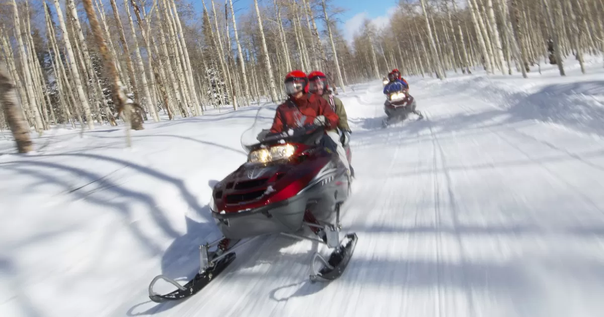 People riding snowmobiles on a snowy trail